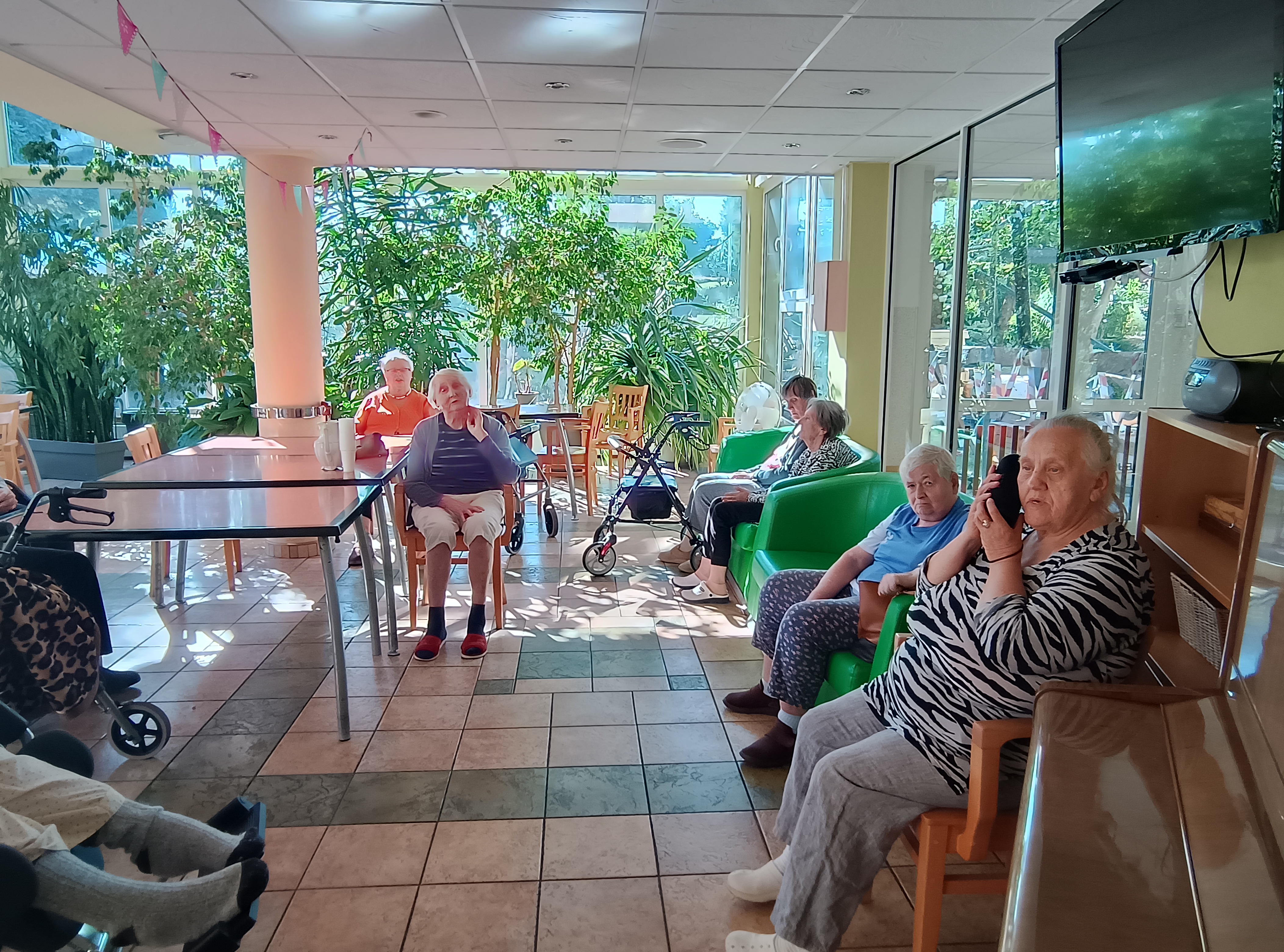 Grupa osób siedzi na kanapach i krzesłach w ogrodzie zimowym