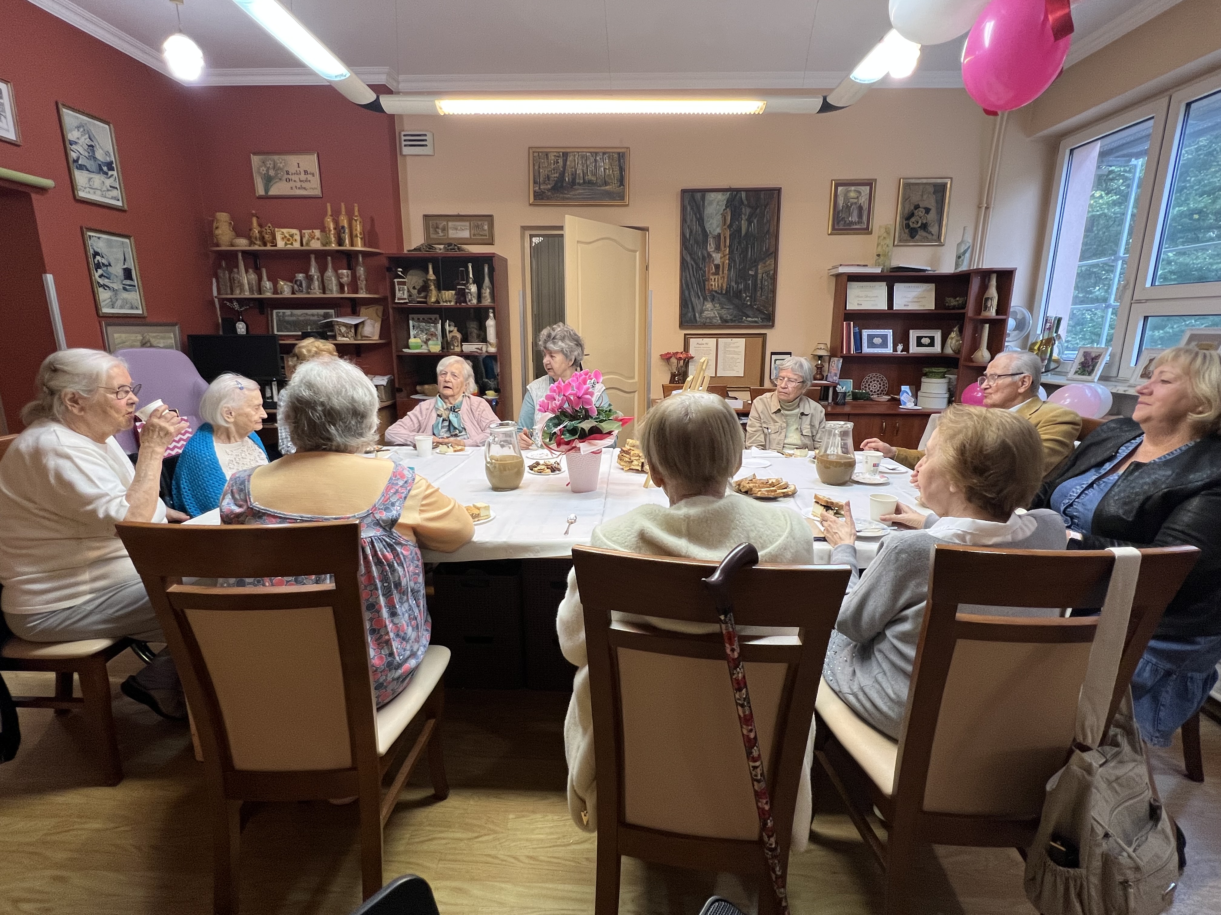 Grupa seniorów wokół stołu, świętująca 101 urodziny mieszkanki