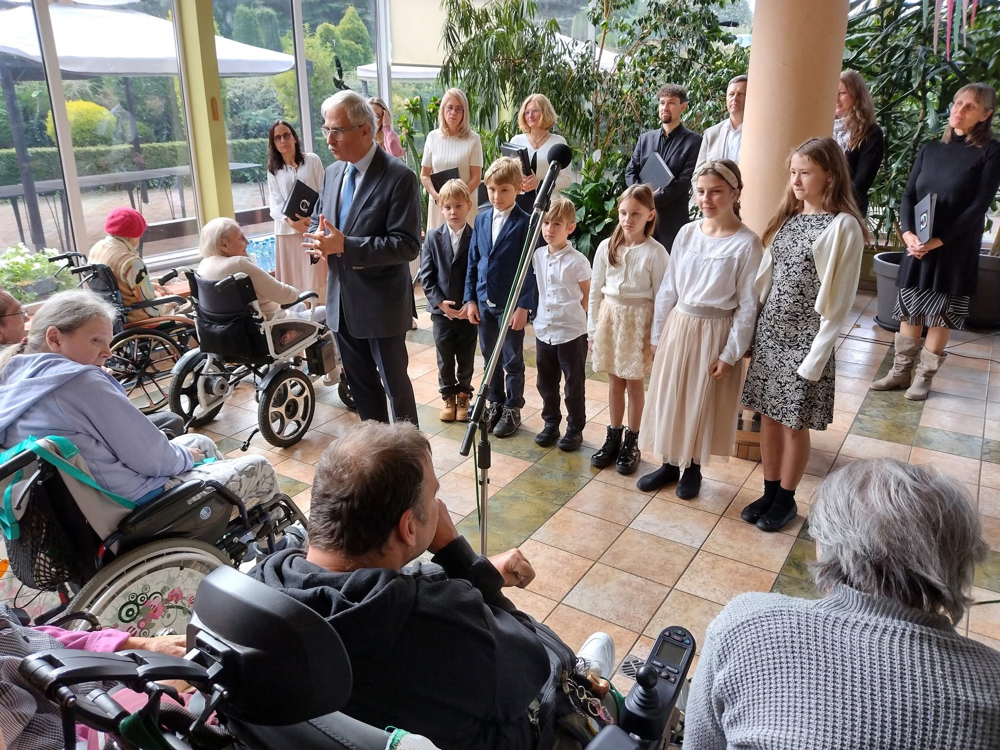 Konferansjer przemawia do pensjonariuszy, w tle chór
