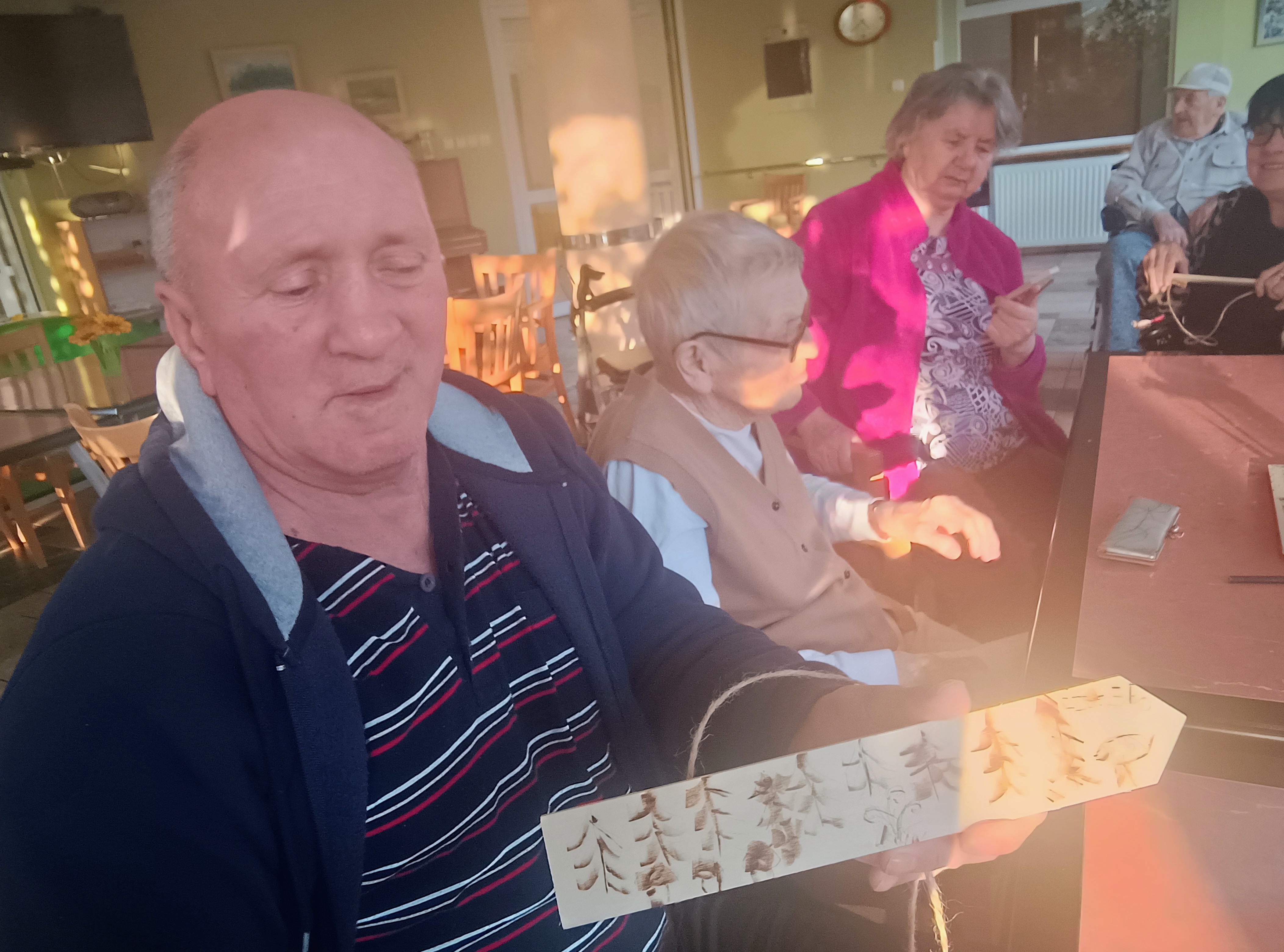 Senior prezentuje swoją pracę plastyczną - wypalanie wzorków w deszczułce
